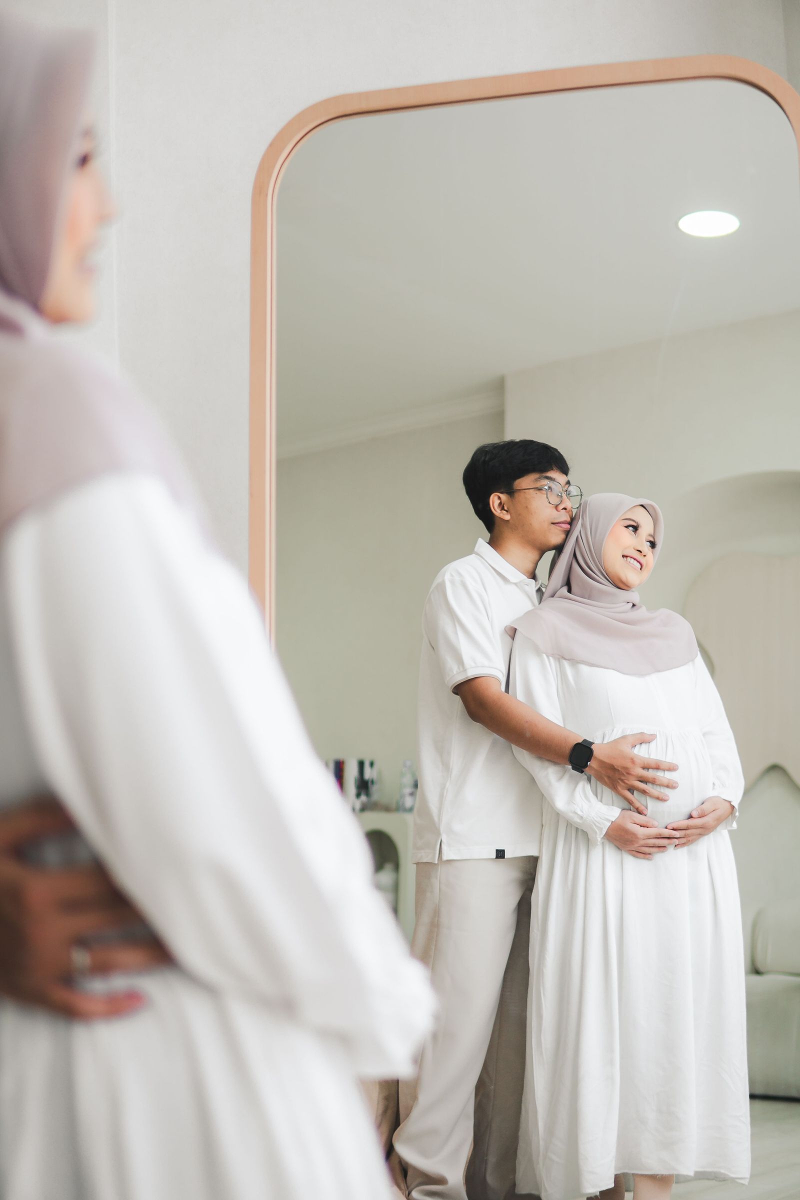 A couple standing together, expecting a baby, reflected in a mirror.